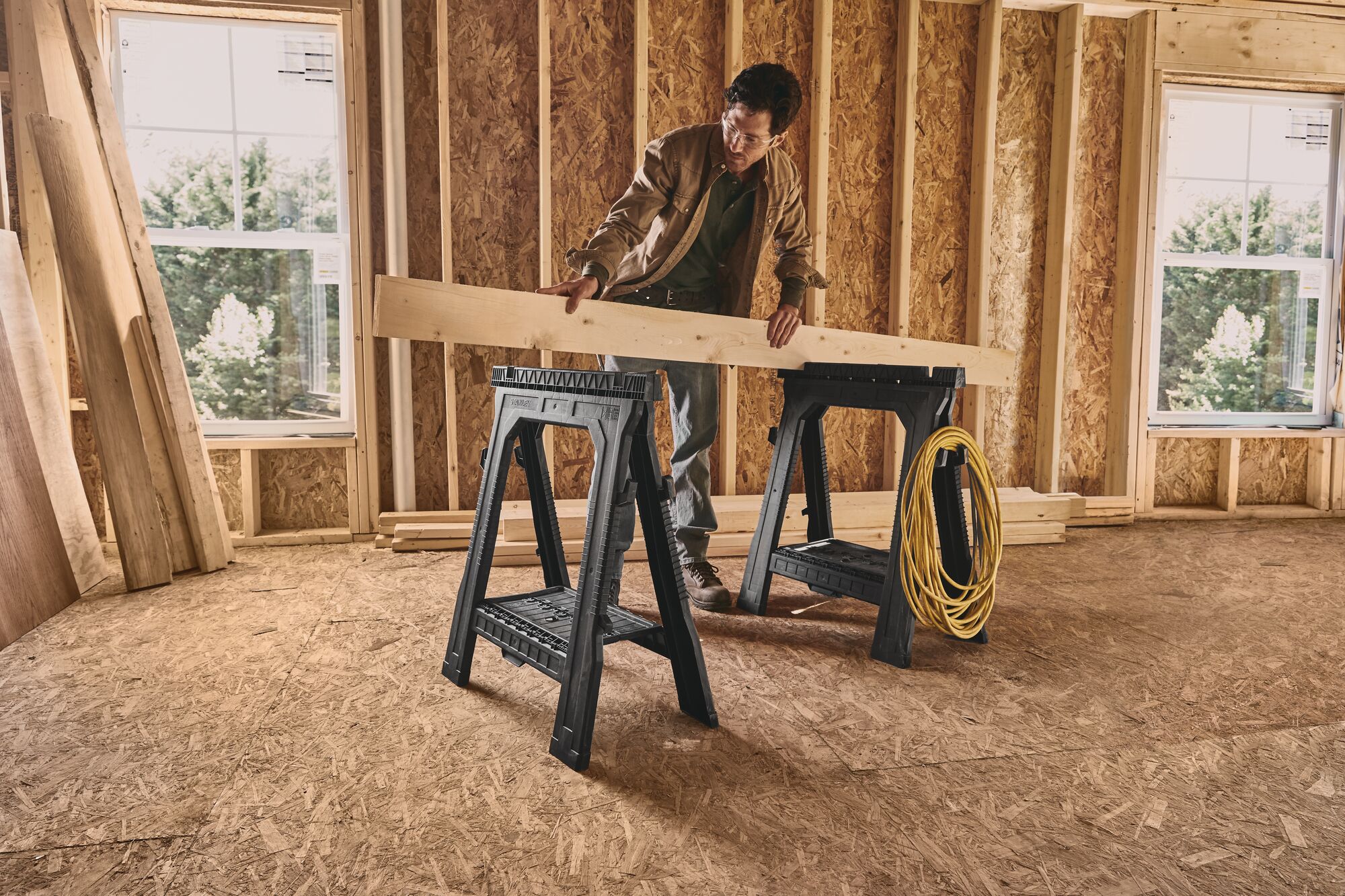 Person using Portable Folding Sawhorse to secure wooden plank at work site.