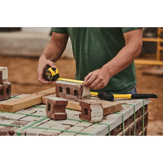 25 foot FATMAX classic tape measure being used by a person to measure length of a brick.