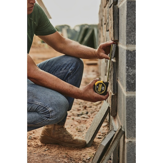 25 foot FATMAX classic tape measure being used by a person to measure brick tile length.