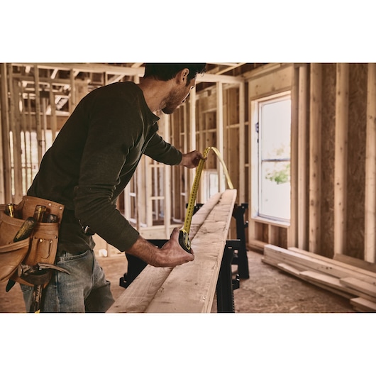 25 foot FATMAX classic tape measure being used by a person to measure length of a wooden plank.