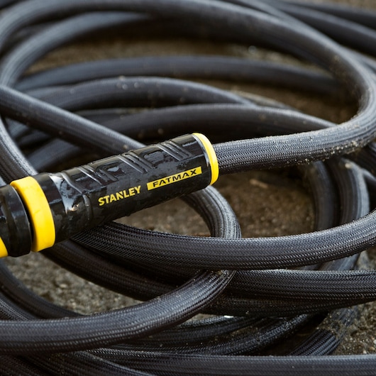 Gray, black, and yellow Stanley FATMAX exojacket hose laying on soil.