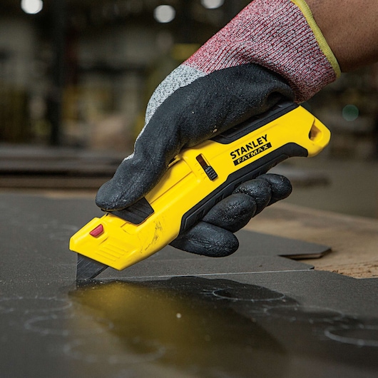 Fatmax auto retract tri slide safety knife being used to cut a sheet.