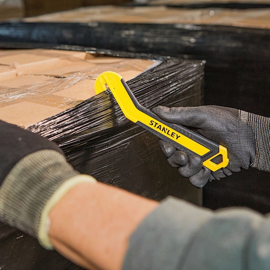 SINGLE SIDED ROUND TIP BI MATERIAL PULL CUTTER being used for cutting plastic packing on cardboard box.